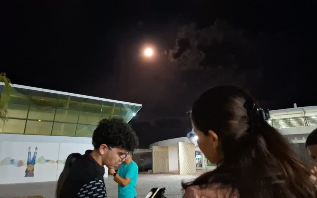 Fenômeno ‘Superlua’ reúne público no Campus Humberto Teixeira  A última superlua de 2025 movimentou o Campus Humberto Teixeira, em Iguatu, na noite desta quinta-feira, 4. A observação integrou ação do Grupo de Estudos em Astronomia Zênite – GEAZ, projeto de extensão do curso de Física da UECE – FECLI voltado à astronomia e à divulgação científica. O grupo busca aproximar escolas, estudantes e comunidades do conhecimento sobre o universo, promovendo atividades práticas, palestras e experiências observacionais. O evento contou com exposição fotográfica da Lua e observação ao vivo do satélite natural por meio de dois equipamentos: uma luneta e um telescópio que permitiam aos visitantes acoplar o próprio celular para registrar imagens. A movimentação foi intensa e rapidamente uma fila se formou ao redor dos instrumentos. A superlua – fenômeno em que o satélite natural parece maior e mais brilhante por estar mais próximo da Terra – encerrou o calendário astronômico do ano e serviu como oportunidade para ampliar o interesse pela ciência na região. O Grupo Zênite segue promovendo ações que aproximam a comunidade da Astronomia e fortalecem a divulgação científica no Centro-Sul do Ceará.  Experiência Representante do Grupo Zênite e aluno do sexto semestre de Física, João Pedro destacou o propósito da iniciativa. “A ideia é que as pessoas tenham um primeiro contato mais direto com a Astronomia. A superlua é um momento especial, e queremos aproveitar para mostrar como a ciência pode ser acessível e despertar interesse em quem talvez nunca tenha usado um telescópio antes”, explicou. A exposição fotográfica, que reuniu registros produzidos pelos integrantes do projeto, foi organizada por Gisele dos Santos, estudante do 4º semestre de Biologia. Ela ressaltou o caráter interdisciplinar das ações do Zênite. “Mesmo sendo da Biologia, encontrei no projeto uma oportunidade de aprender mais sobre Astronomia e ajudar na divulgação. Meu marido é do curso de letras e também colabora com zênite. É um trabalho que envolve diferentes cursos e isso enriquece demais a experiência”, afirmou. Entre os visitantes, Ana Beatriz, estudante do 4º semestre de Pedagogia, contou que estava passando pelo campus quando decidiu entrar na fila para observar a superlua pelo equipamento. “Parecia algo simples, mas quando olhei pelo telescópio fiquei encantada. Ver a Lua tão de perto é totalmente diferente do que vemos a olho nu”, relatou.